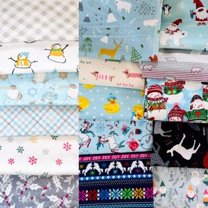May include: A collection of fabric scraps featuring various winter holiday themes. The fabrics include a variety of colors and patterns, such as snowflakes, reindeer, snowmen, and penguins. The fabrics are arranged in a stack, with the top fabric being a light blue fabric with a white snowflake pattern.