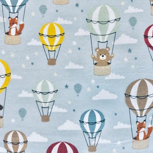 May include: A light blue fabric with a repeating pattern of hot air balloons, clouds, and stars. The balloons are in various colors, including yellow, green, and red, and feature cute animal passengers like a fox, bear, and dog.