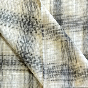 May include: Close-up of a beige and black plaid fabric with a textured weave. The fabric is folded in half, showing the pattern on both sides.