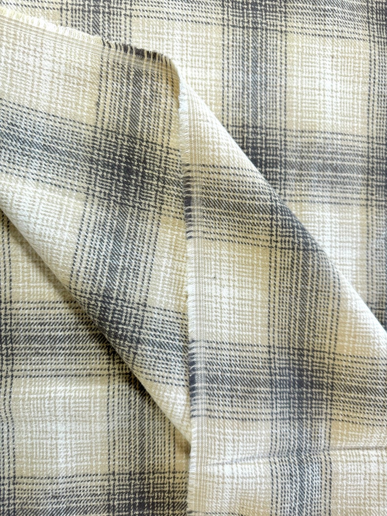 May include: Close-up of a beige and black plaid fabric with a textured weave. The fabric is folded in half, showing the pattern on both sides.