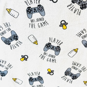 May include: White fabric with a repeating pattern of gray game controllers, baby bottles, and pacifiers. The text "PLAYER HAS JOINED THE GAME" is also included in the design. The theme is baby and gaming.