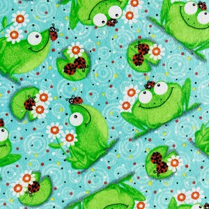 May include: A blue fabric with a repeating pattern of green frogs, white flowers, and red ladybugs. The frogs are smiling and have big eyes. The flowers are simple and have five petals. The ladybugs are small and have black spots.