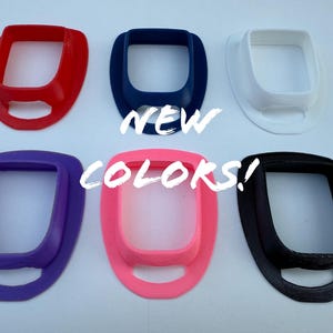 May include: Six colorful, oval-shaped objects in red, navy blue, white, purple, pink, and black. The text "NEW COLORS!" is written across the image in white. The objects have a rectangular opening in the center.