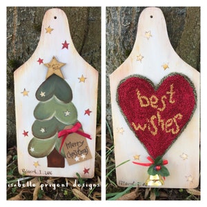 May include: Two wooden Christmas decorations. The first decoration is painted with a green Christmas tree and a red and white tag that says "Merry Christmas". The second decoration has a red heart with the words "best wishes" in gold thread. Both decorations have gold stars and red stars painted on them.