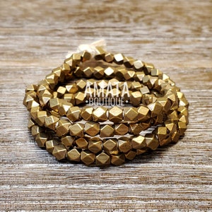 May include: A stack of gold-colored metal bead bracelets. The beads are faceted and have a geometric shape.