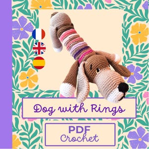 Op de afbeelding: Een gehaakt hondenspeeltje met een lange, gestreepte body en floppy oren. De hond is bruin en wit, met een zwarte neus. De tekst "Dog with Rings" en "PDF Crochet" staan op de afbeelding.