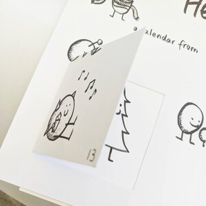 May include: A white calendar with whimsical black ink illustrations. The open page shows a drawing of a bird with musical notes and the number 13. Other drawings include a snowman and a creature wearing a scarf.