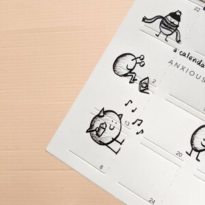 May include: A white calendar page with whimsical black ink illustrations. The drawings depict small, round characters in various poses, some with musical notes. The text "a calendar ANXIOUS" is visible. The calendar has numbered boxes for each day.