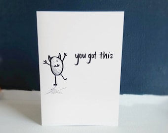 May include: A white greeting card featuring a black ink hand-drawn illustration of a small oval-shaped monster with horns and raised arms, accompanied by the handwritten black text "you got this" and the brand name "ANXIOUSLITTLEMONSTERS".