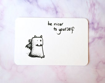 Könnte beinhalten: Eine weiße Karte mit einer Schwarzweißillustration eines kleinen Drachen mit Flügeln. Der Text "be nicer to yourself" ist in schwarzer Tinte geschrieben.