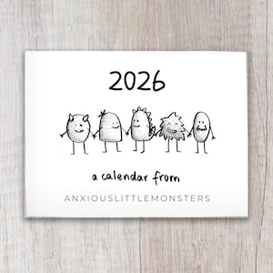 Könnte beinhalten: Ein weißer Kalender für das Jahr 2026, mit der Jahreszahl in großem schwarzem Text. Unter der Jahreszahl halten fünf Cartoon-Monster Händchen. Der Text "a calendar from ANXIOUSLITTLEMONSTERS" ist ebenfalls vorhanden.