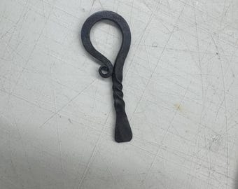 Puede incluir: Abridor de botellas de metal oscuro forjado a mano con un mango retorcido y una parte superior en forma de lazo. El abridor tiene un extremo plano en forma de paleta para hacer palanca. El diseño es simple y rústico.