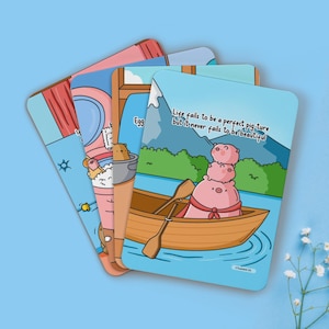 May include: Four illustrated cards with a cute pig theme. The cards feature a pig in a boat, a pig taking a bath, a pig eating an egg, and a pig wearing a crown. The text on the cards reads "Life fails to be a perfect pig-ture but it never fails to be beautiful."