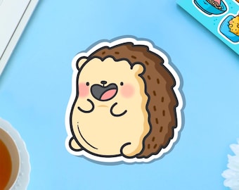 Puede incluir: Una pegatina con un erizo de dibujos animados con un cuerpo marrón claro, una espalda espinosa marrón y una cara sonriente. El erizo tiene una nariz negra y mejillas rosadas. La pegatina está sobre una superficie azul claro.