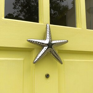 May include: A silver starfish door knocker on a yellow door.