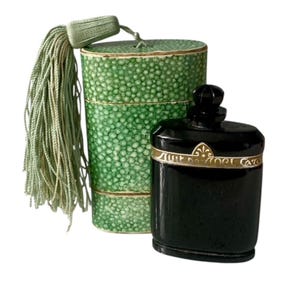 May include: A black perfume bottle with gold trim and a matching green dotted box with a tassel. The bottle has a rounded top and a gold band with text. The box is cylindrical and has a matching green tassel.