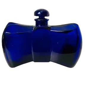 Puede incluir: Una botella de vidrio azul cobalto con una forma única de corbata de lazo. La botella tiene un pequeño tapón redondeado. El diseño es simétrico, con lados curvos y una base plana. El vidrio parece liso y reflectante.