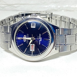 May include: A silver-toned Orient watch with a blue dial. The watch features a date display at the 3 o'clock position and a silver band. The watch face has silver hour markers and hands. The watch is water resistant to 50m.