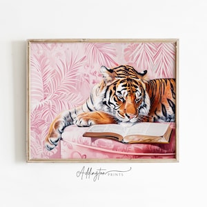 May include: A framed print featuring a tiger resting on a pink sofa, engrossed in a book. The tiger has orange and black stripes. The background is a pink floral pattern. The print is labeled "Addington Prints".