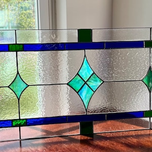 May include: A stained glass window panel with a geometric design featuring blue, green, and clear glass.