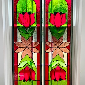 May include: Two stained glass window panels with a floral design. The panels feature red, green, and copper-colored glass. The design includes red tulip-like flowers, green leaves, and copper-colored starbursts, all set against a red and white striped background.
