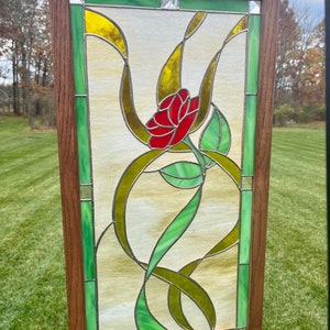 May include: A stained glass window panel featuring a red rose with green leaves and gold vines. The panel is framed in a dark wood frame.
