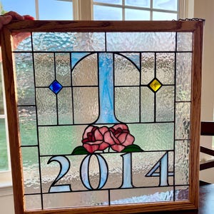 May include: A stained glass window with a blue and white letter T, two pink roses, and the year 2014 in white.
