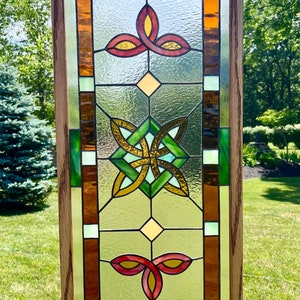 May include: A stained glass window with a Celtic knot design in green, gold, and brown. The window is framed in oak wood and has a light brown background.