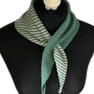 May include: A triangular knit scarf featuring a two-tone design. One side displays a solid sage green colour, while the other side showcases a pattern of thin, alternating sage green and off-white horizontal stripes. The scarf is tied at the front.