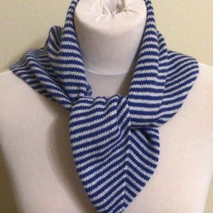 May include: A blue and white striped knitted scarf is displayed on a mannequin. The scarf features alternating blue and white horizontal stripes. The scarf is looped around the mannequin's neck and tied in a knot at the front.