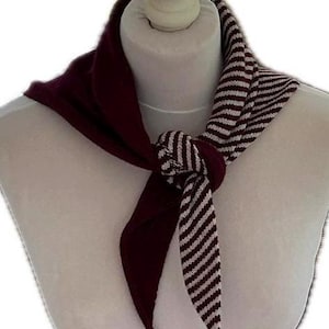 May include: A triangular scarf tied in a knot around a mannequin neck. One side of the scarf is solid dark burgundy, whilst the other side features a pattern of thin, alternating white and dark burgundy stripes. The fabric appears to be knit.