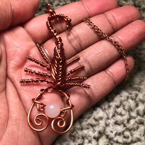 May include: A copper wire scorpion pendant with a pink stone. The scorpion is detailed with wire wrapped around its body and legs. The pendant is attached to a copper chain.