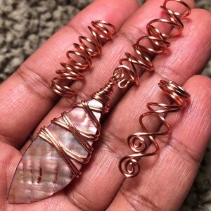 May include: Three copper wire hair coils, one with a large iridescent shell wrapped in copper wire. The coils are designed to help style hair.