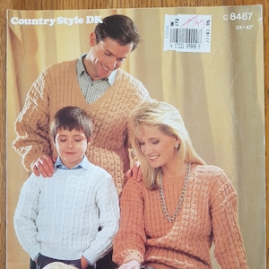 Op de afbeelding: Afbeelding van een familie in gebreide truien in perzik, wit en bruin. De afbeelding komt uit een vintage breipatroonboek, met de tekst "Country Style DK" bovenaan. Het patroon is voor maten van 61-107 cm.