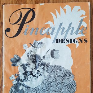 Op de afbeelding: Vintage boekomslag getiteld "Pineapple Designs" op een oranje achtergrond. De omslag toont een bloemstuk en een gehaakte doily. Tekst bevat "Doilies, Tafelkleden, Spreien, Lopers."