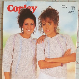 Op de afbeelding: Twee vrouwen dragen witte truien met blauwe en paarse strepen en witte shorts. De truien zijn gebreid met een kabelsteek. De tekst op de afbeelding is "Cotton 'n Cream DK and Hint of Linen DK".