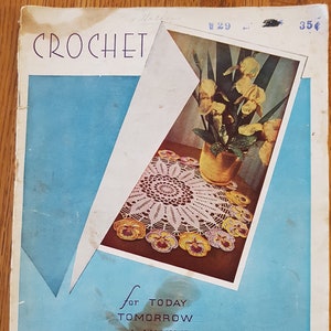 Op de afbeelding: Een vintage haakboekomslag met een gehaakt tafellaken met een bloemenmotief. De omslag is blauw met witte tekst die "CROCHET for TODAY TOMORROW and ALWAYS" luidt. Het boek is getiteld "LILY DIRECTION BOOK 1700" en kost "25 cent".