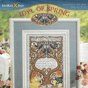 Könnte beinhalten: Stickmuster für ein gerahmtes Stickbild mit dem Titel "An Idyl of Spring". Das Design zeigt einen Baum mit Vögeln, Blumen und zwei Figuren. Der Text lautet "For lo! The winter is over and past and the singing birds have come spring is here with her masque of flowers and love is abroad in her leafy bowers."