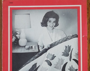 Könnte beinhalten: Ein Schwarzweißfoto einer Frau, die eine Steppdecke mit Tulpenmuster hält. Die Steppdecke ist weiß mit schwarzen Tulpen und Blättern. Der Text "QUILT BOOK COLLECTION 1" ist auf dem Buchcover gedruckt.