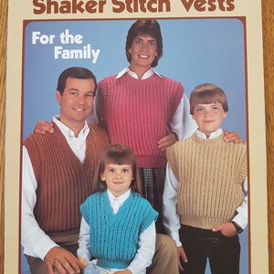 Puede incluir: Un folleto vintage titulado "Shaker Stitch Vests" de Leisure Arts. La portada presenta a una familia con chalecos de punto en marrón, rosa, azul y beige. El texto en la portada dice "For the Family" y "Designed by Barbara B. Rondeau."