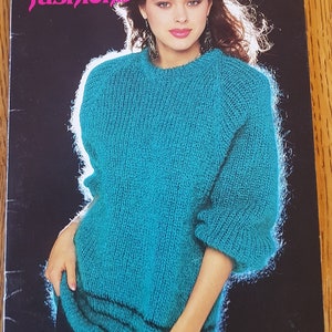Könnte beinhalten: Ein türkisfarbener Strickpullover mit Rundhalsausschnitt und langen Ärmeln. Der Pullover hat ein Rippenmuster und einen kontrastierenden schwarzen Streifen am Saum. Der Pullover ist in einem Vintage-Strickmusterbuch abgebildet.