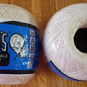 Puede incluir: Dos ovillos blancos de 1000 yardas de hilo de crochet de algodón mercerizado Aunt Lydia's. La etiqueta en uno de los ovillos dice "Aunt Lydia's 1000 YARDS Mercerized Cotton Crochet Exceptionnelle - Algodon Mercerizado".