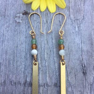 May include: Gold dangle earrings with green, white, and brown beads and a gold bar pendant.