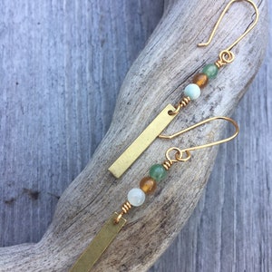 May include: A pair of gold dangle earrings with a long, thin, rectangular bar charm and three beads in shades of green and amber.