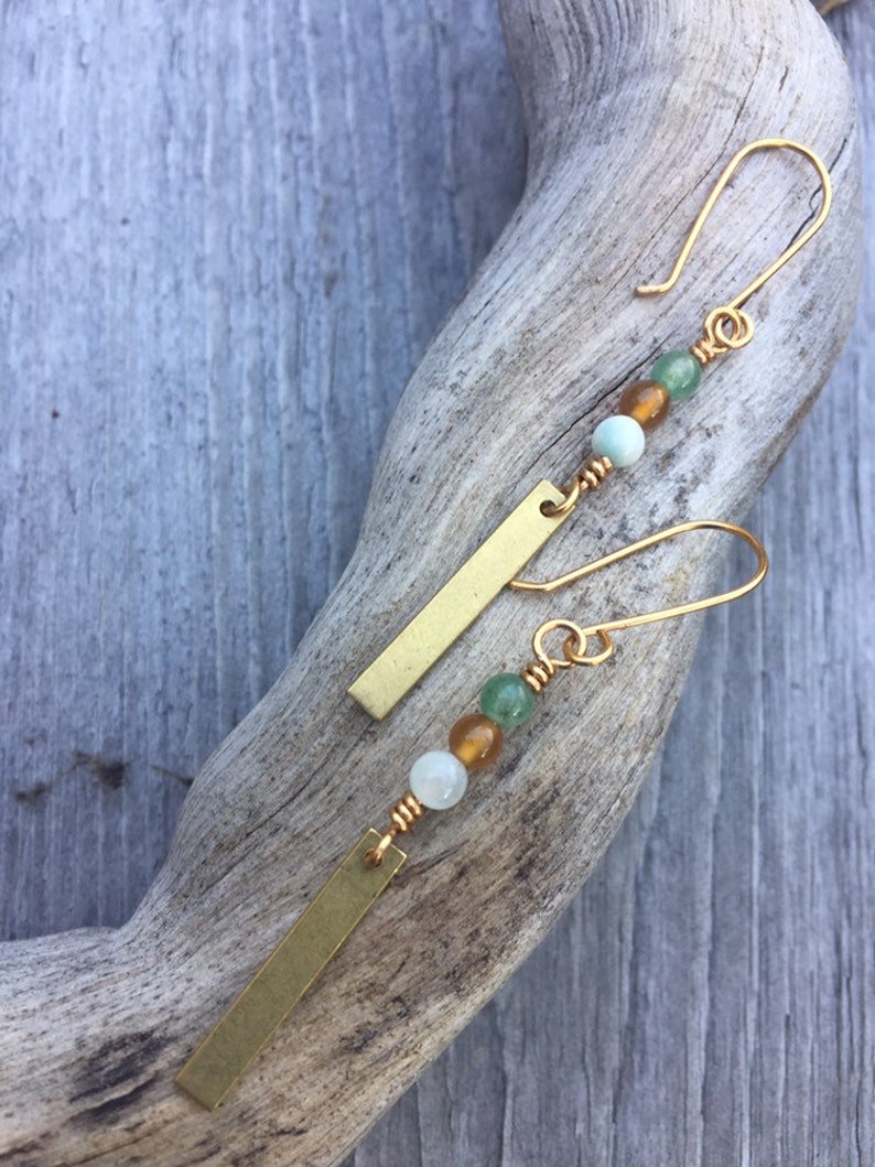 May include: A pair of gold dangle earrings with a long, thin, rectangular bar charm and three beads in shades of green and amber.