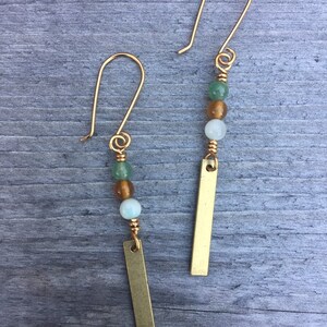 May include: A pair of gold earrings with green, white, and brown beads and a gold bar pendant.