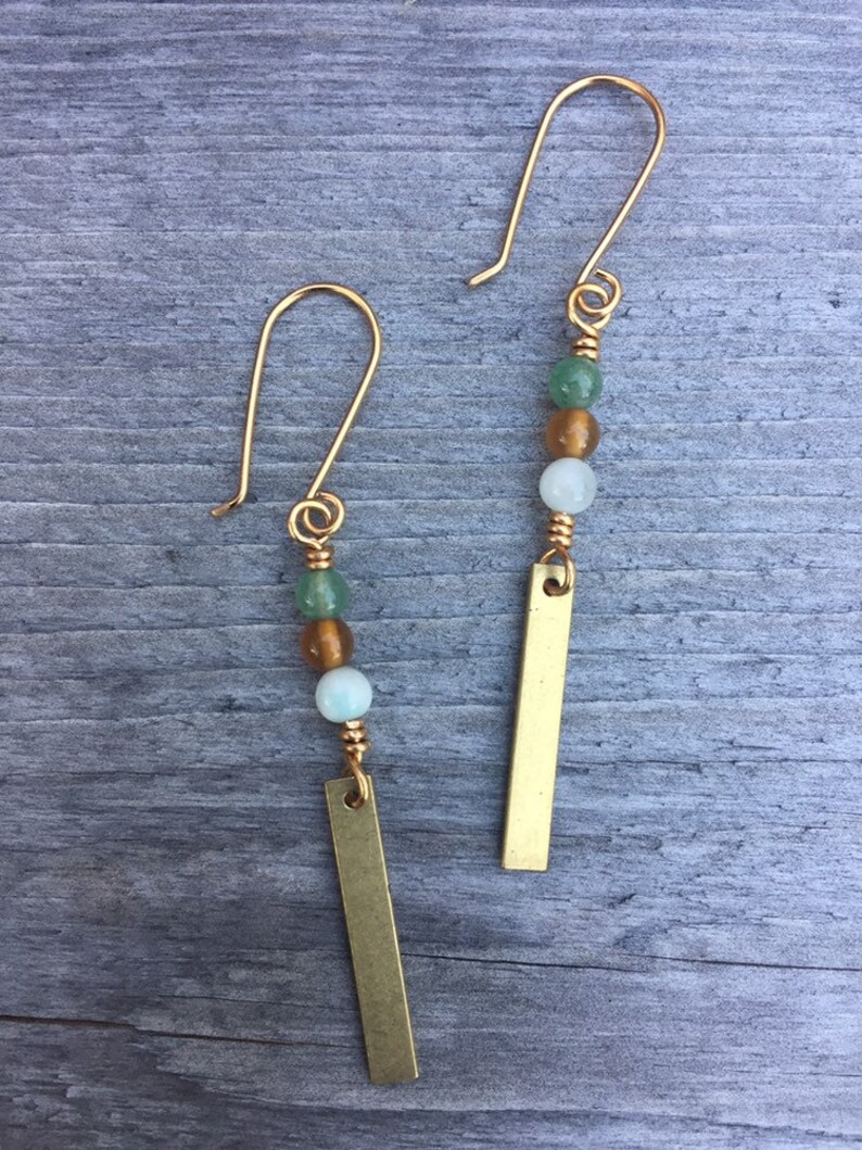 May include: A pair of gold earrings with green, white, and brown beads and a gold bar pendant.
