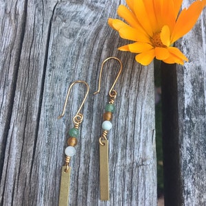 May include: A pair of gold dangle earrings with green and white beads and a gold bar pendant.