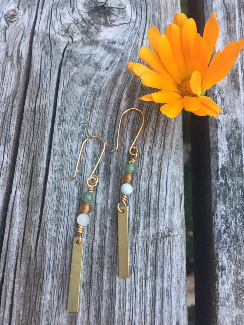 May include: A pair of gold dangle earrings with green and white beads and a gold bar pendant.