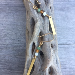 May include: Gold earrings with a small gold bar charm and three beads: green, brown, and white.